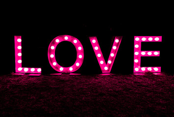 black night with the word and text love written in brightly lit letters in pink horizontal view with copy space