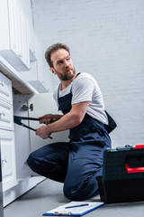 repairman in working overall fixing sink with pair of nippers in kitchen