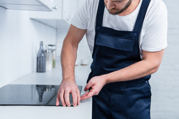 cropped shot of handyman in working overall fixing oven in kitchen