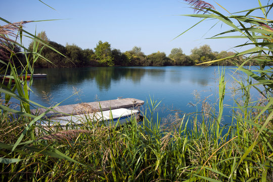 A rowing boat moored by a small jetty on a lake in summer sunshine