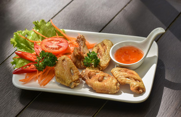 Crispy fried chicken wings in Thai style cooking served with sweet and hot sauce. The dish decorated with colorful vegetables and lighted up by morning light.