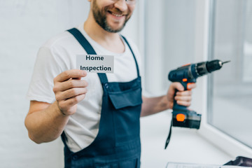 partial view of male craftsman holding electric drill and showing card with lettering home...