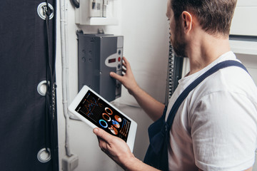 male electrician holding digital tablet with graphs on screen and checking electric box
