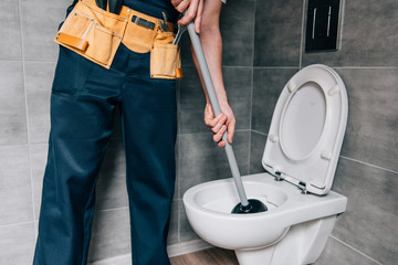partial view of male plumber using plunger and cleaning toilet in bathroom