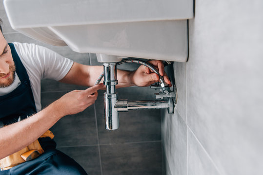 partial view of male plumber in working overall fixing sink in bathroom