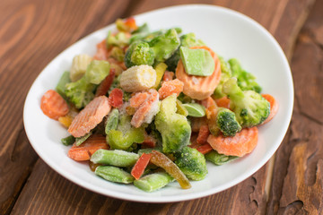 Frozen various vegetables on a plate on a wooden background.