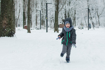 Fototapeta na wymiar A little boy runs through the snow in the park.