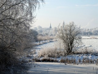 Verschneite Bäume im Park links der Weser in Bremen und mit der Kirche St. Georg in Bremen-Huchting im Hintergrund