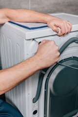 cropped image of male handyman repairing washing machine in bathroom