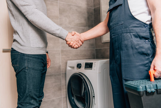 cropped image of male handyman with toolbox shaking hands with owner in bathroom