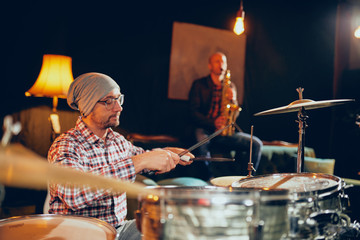 Two men playing drums and saxophone in home studio.