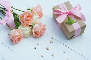 Lovely soft orange pink color rose tied by pink ribbon and brown gift box on white wood table background, sweet valentine present concept