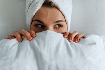 Closeup portrait of attractive young woman lying down on the bed and awake. Top view beautiful...