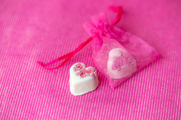 sweet white heart-shaped chocolates on a pink background