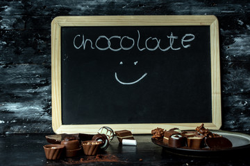 different, sweet pralines of dark, milk and white chocolate on a dark, wooden background, next to...