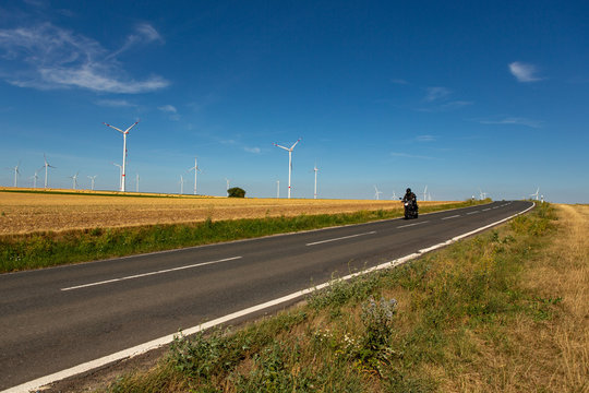 A motorcyclist in an agricultural landscape with wind turbines in the background
