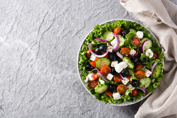 Fresh Greek salad in Plate with black olive,tomato,feta cheese, cucumber and onion on gray background. Top view. Copyspace