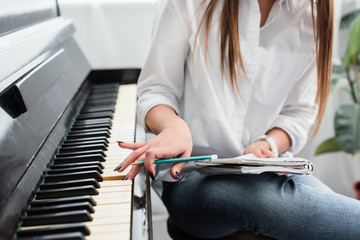 cropped view of girl in white shirt with notebook playing piano and composing music at home