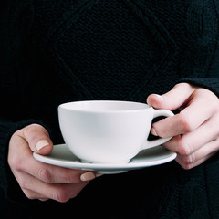 A woman in a black sweater holds a white mug in her hands. Template for text or design