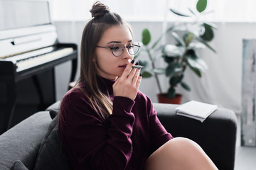 beautiful girl sitting on couch and smoking marijuana joint in living room © LIGHTFIELD STUDIOS