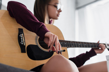 selective focus of girl sitting, holding marijuana joint and playing guitar at home