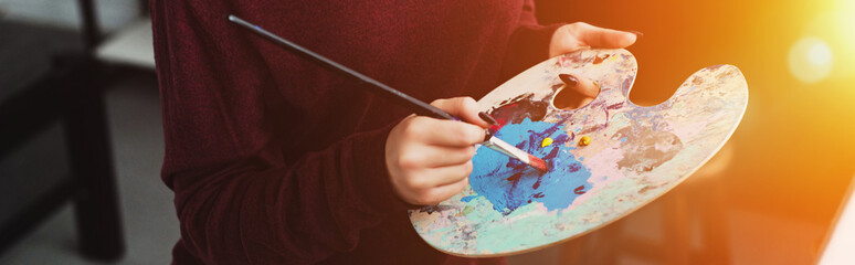partial view of girl holding paintbrush with palette and painting at home with backlit