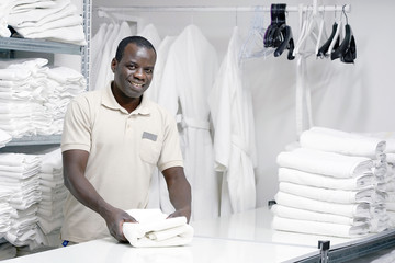  African male hotel worker folds a clean white towel. Hotel staff workers. Hotel linen cleaning...