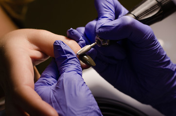 Closeup shot of master in rubber gloves applying an electric nail file drill to remove the nail polish in the beauty salon. Perfect nails manicure process with flying dust or debris