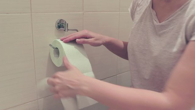 Unrecognizable woman, sitting on a toilet and rewind and tear off a toilet paper. Concept image of digestive problems and difficulties in the toilet