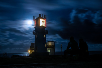 lighthouse in moonlight with two people in front