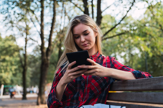 Young woman sitting on bench outdoors using mini tablet