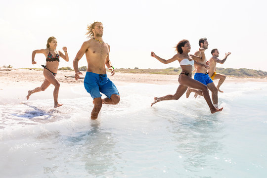 Group of friends having fun on the beach, running into the water