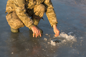 Naklejka premium The guy on the winter fishing at the hole catches a small fishing pole. Closeup of a hand with a winter fishing rod.