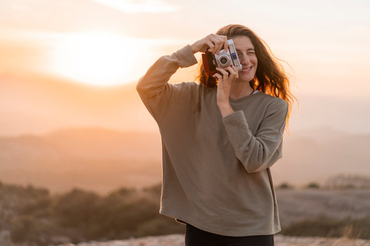 Spain, Barcelona, Natural Park of Sant Llorenc, woman taking a picture with vintage camera at sunset