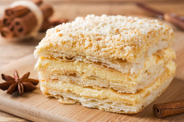 Layered cake with cream Napoleon millefeuille vanilla slice with cinnamon and anise on wooden background.