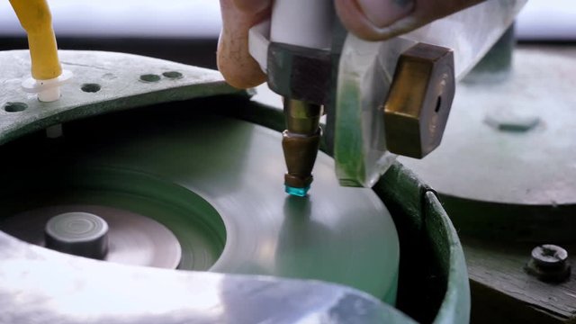 An gemstone cutter polishes a emerald on a faceting machine with chromium oxide in a cutting and polishing workshop.