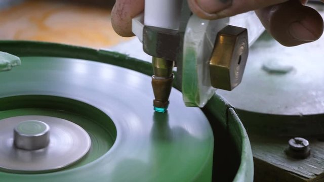 An gemstone cutter polishes a emerald on a faceting machine with chromium oxide in a cutting and polishing workshop.