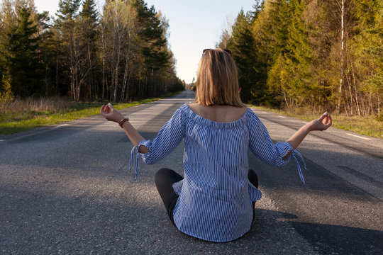 Road to inner peace. Woman sitting in lotos possition on the reoad and meditating. Yoga lifestyle. Zen contemplation