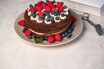 homemade chocolate cake, with raspberries and blueberries on alight backdrop