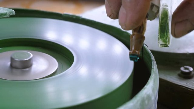 An gemstone cutter polishes a emerald on a faceting machine with chromium oxide in a cutting and polishing workshop.
