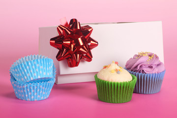 A gift box with delicious baked cupcakes and blue molds on pink background