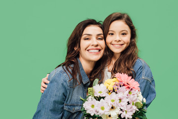 smiling mother and daughter with flowers looking at camera isolated on green