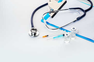 Pills spilling out of pill bottle syringe thermometer and stethoscope on white background