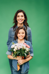 mother and daughter looking at camera and holding flower bouquet isolated on green