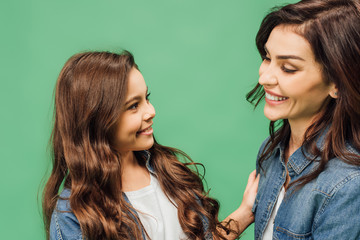 portrait of happy mother and daughter smiling and looking at each other isolated on green