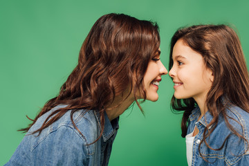 happy mother and daughter looking at each other isolated on green