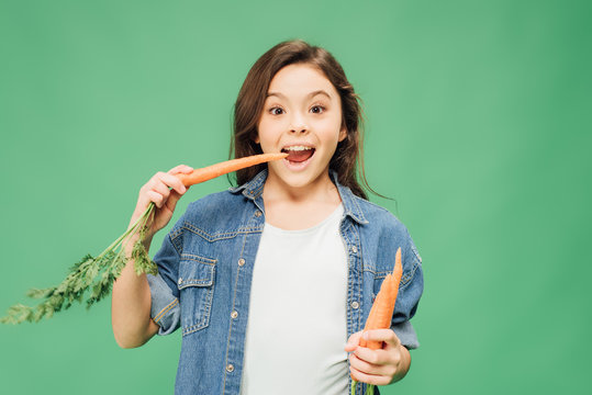 child eating carrots and looking at camera isolated on green