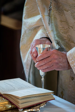 hands of Greek Orthodox priest holding communion chalace