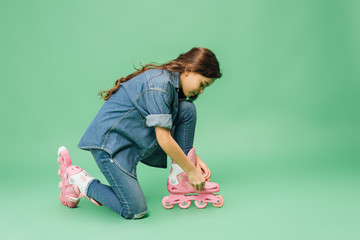 child in denim putting on roller blades on green background
