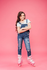 Naklejka premium happy child in overalls with arms crossed wearing rollerblades on pink background